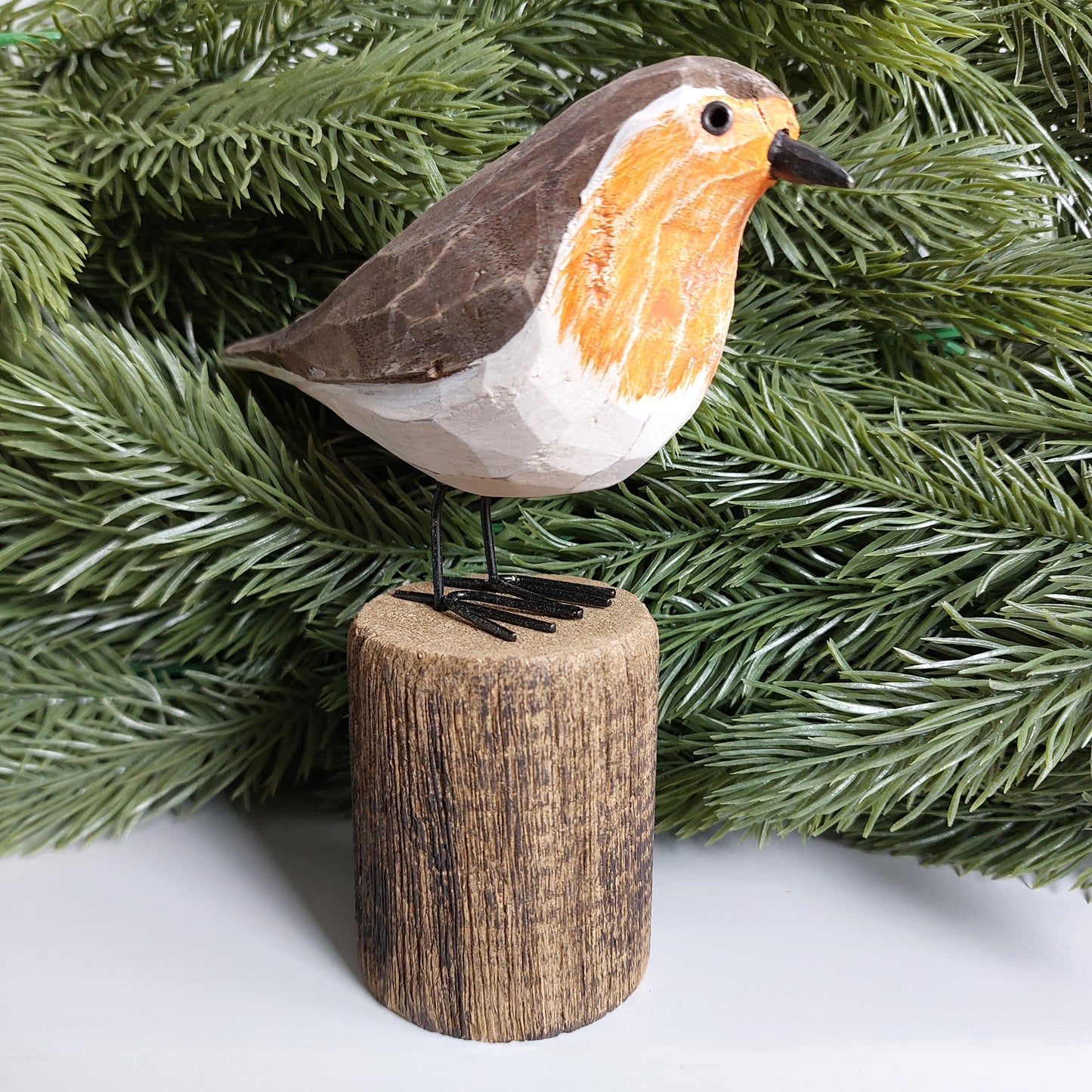 Decorative robin bird figurine on a wooden stand with green faux foliage in the background