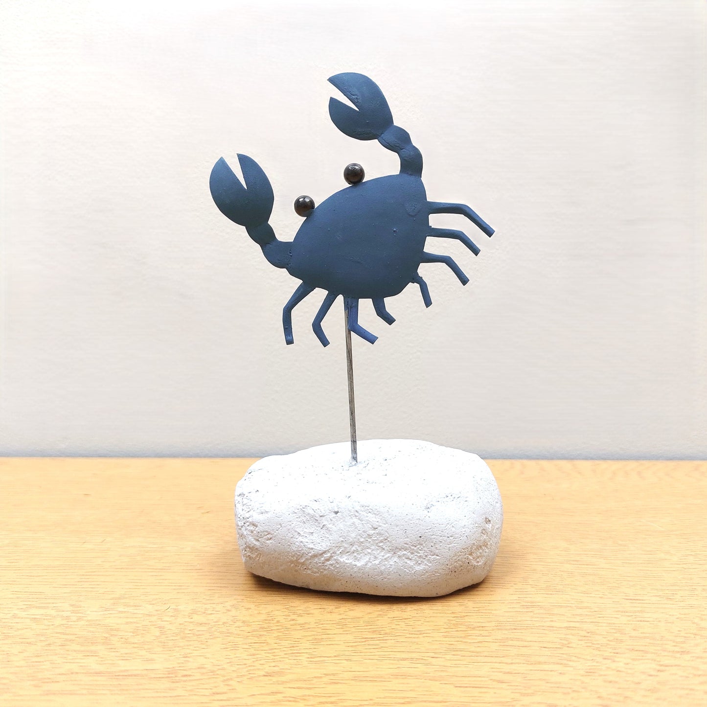 Blue crab-shaped figurine on a white rock against a light background