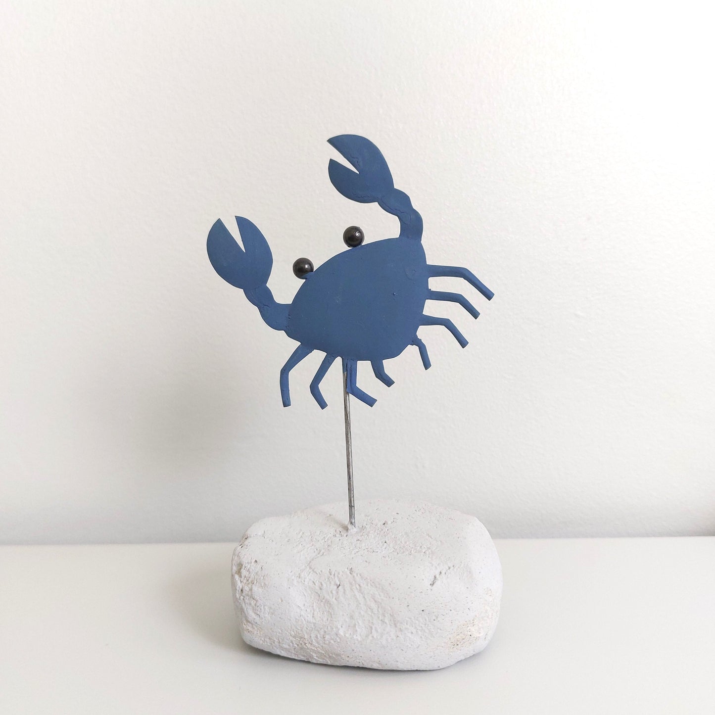 Blue crab-shaped decorative item on a white rock against a light gray background