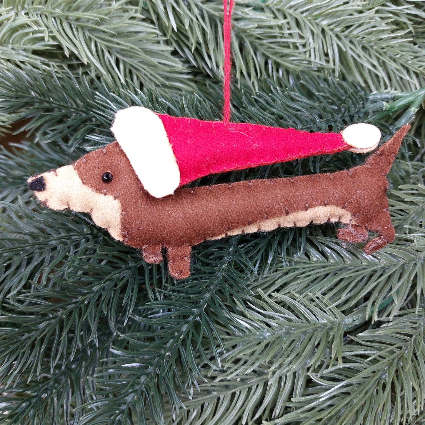 Dog-shaped felt Christmas ornament with a Santa hat on a green tree.
