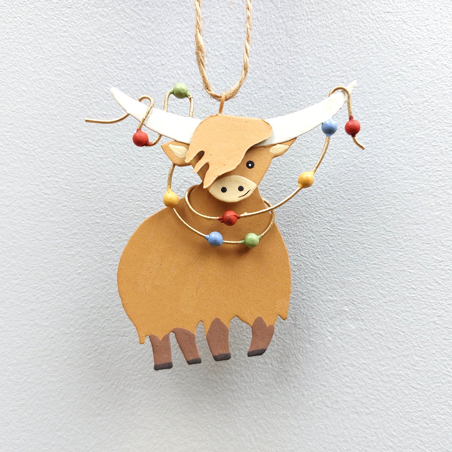 Decorative metal ornament shaped like a highland cow with colorful Christmas lights on a light gray background