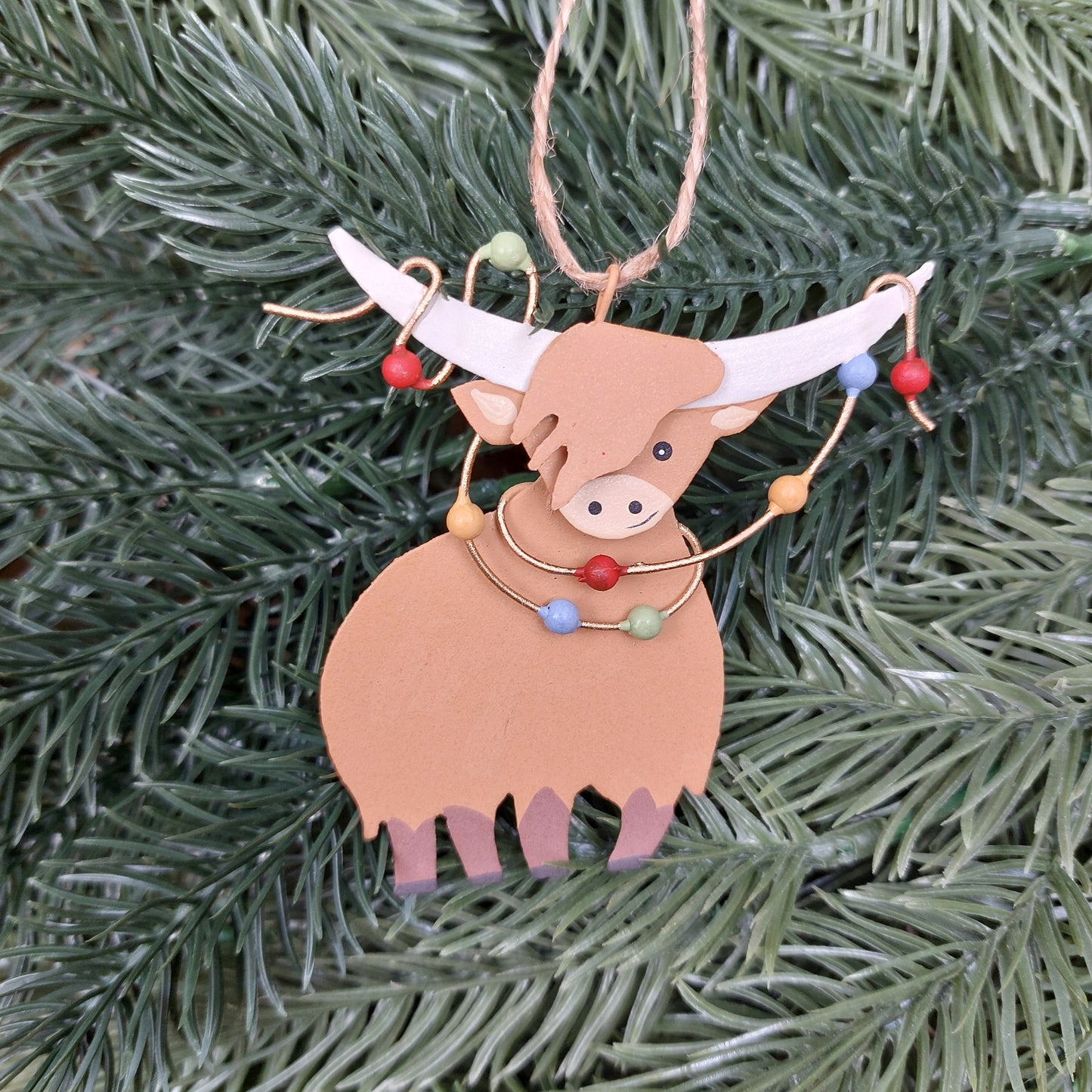 Decorative highland cow ornament with lights on a Christmas tree.