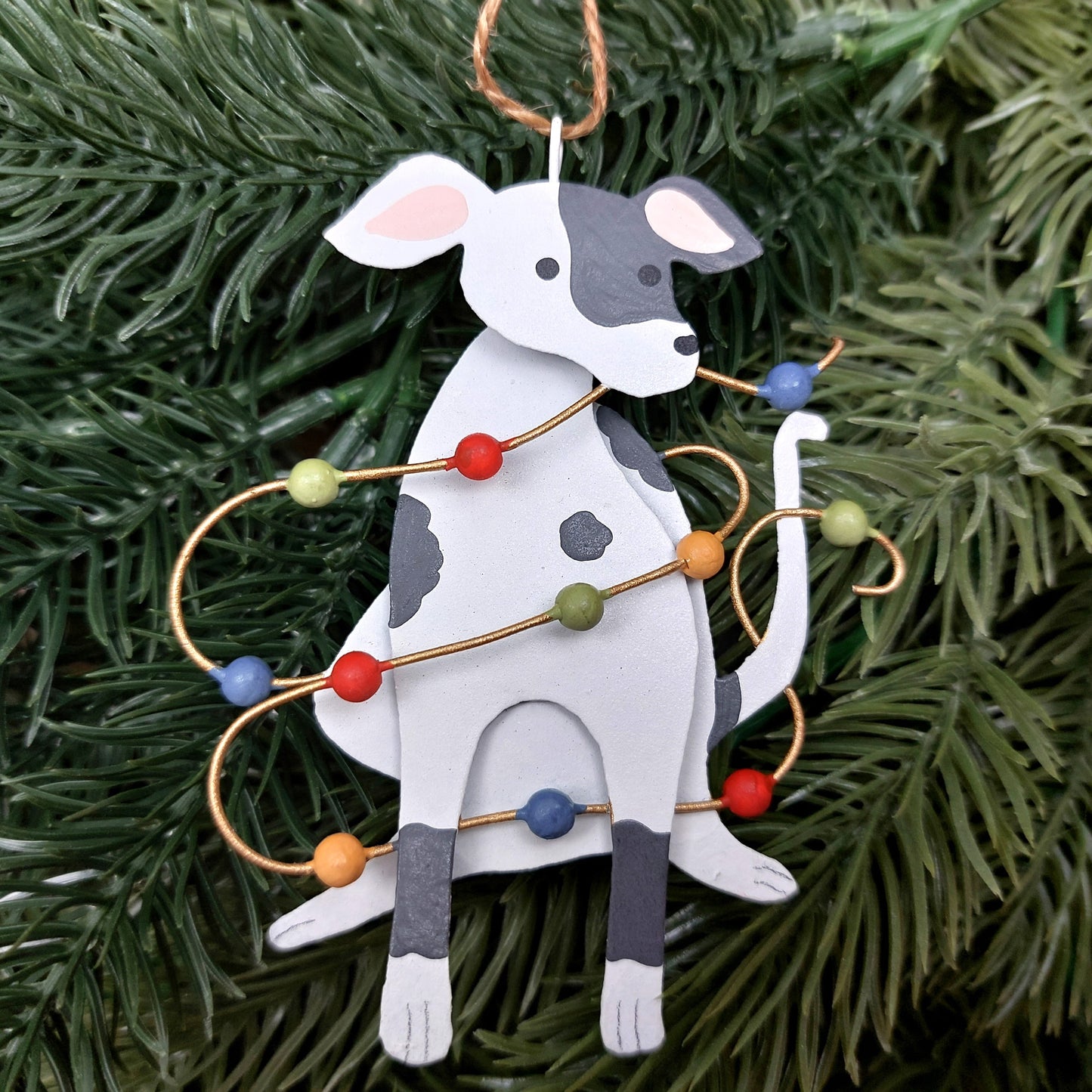 A metal spotty dog with a jute string and Christmas lights against a Christmas tree