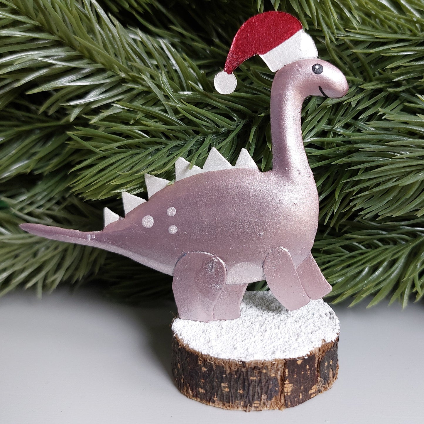 Metal Stegosaurus figurine wearing a Christmas hat on a wooden block against a faux green spruce garland