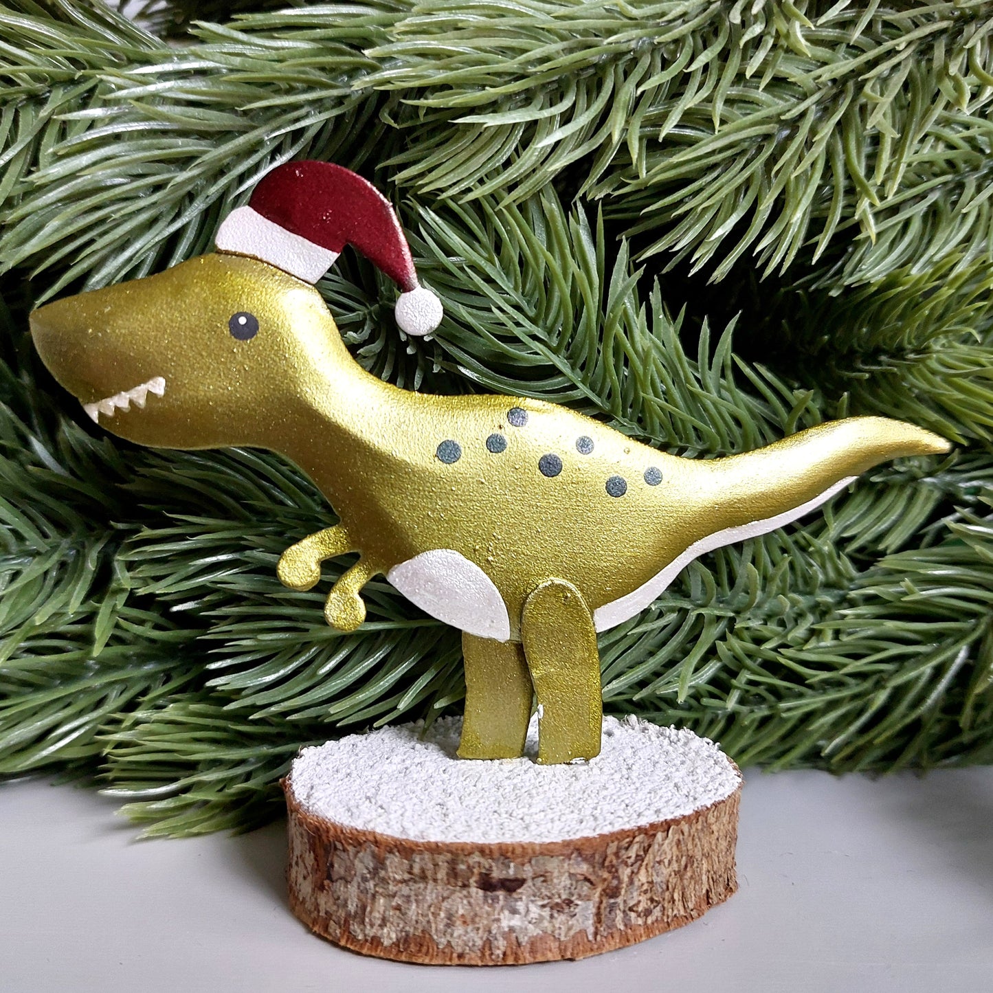 A metal t-rex wearing a Christmas hat on a wooden base against a faux green garland