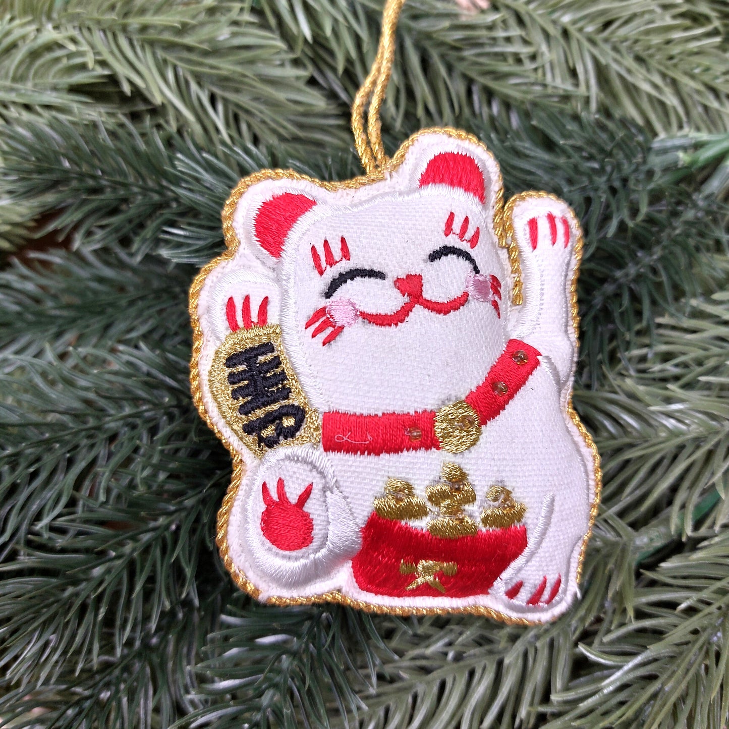 Decorative lucky cat embroidered ornament on a faux green pine spruce branch