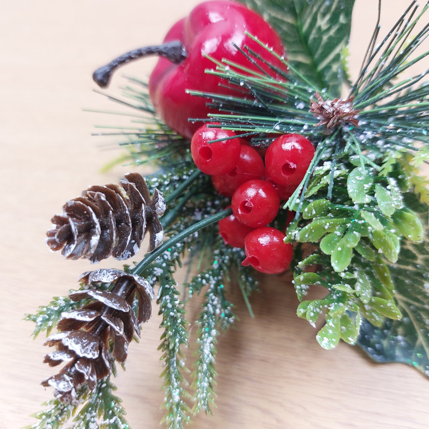 Decorative artificial arrangement with red berries, pine cones, and greenery on a wooden surface