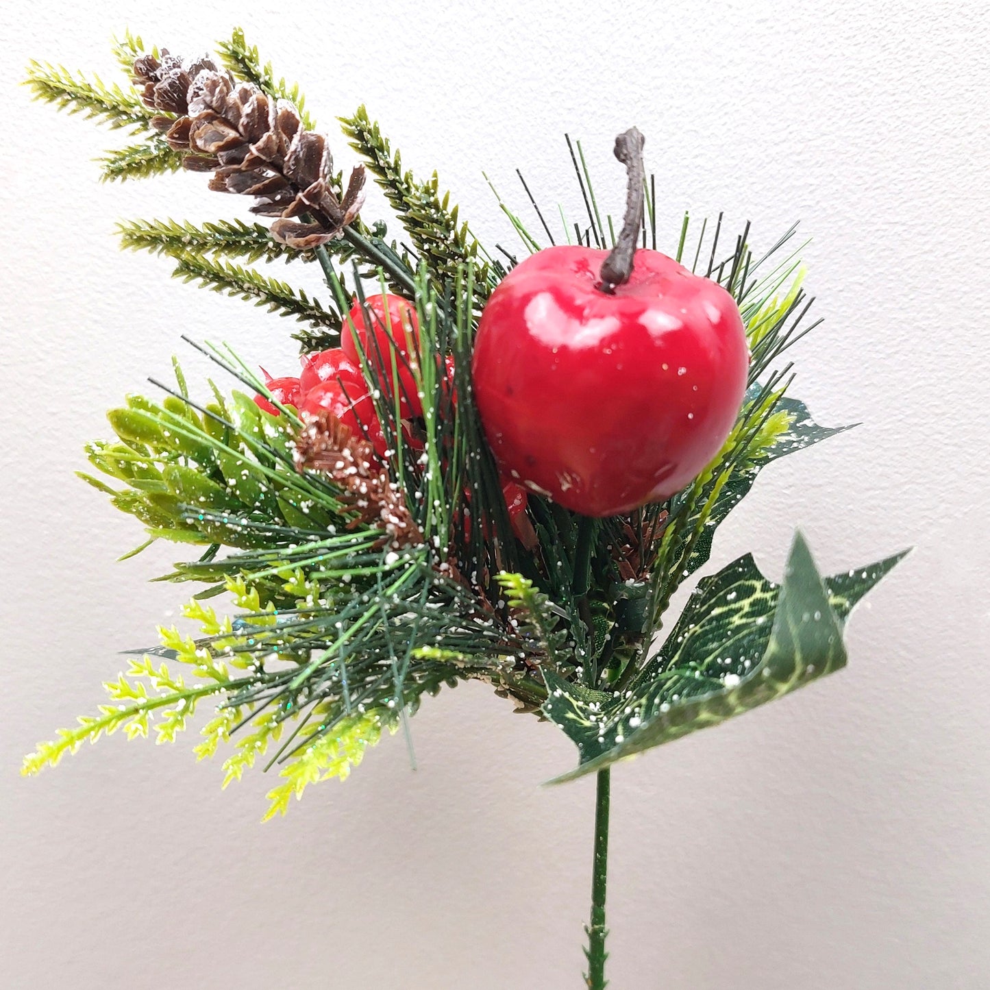 Decorative artificial arrangement with red apples, berries and greenery on a white background