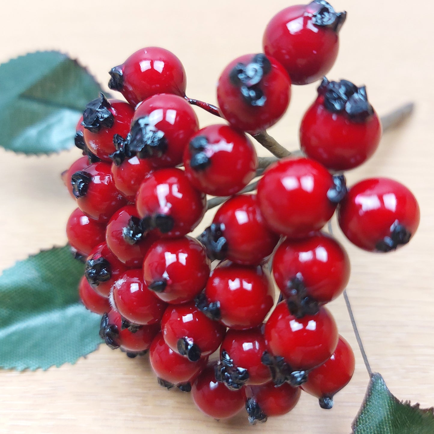 Close-up of artificial red berries with green leaves on a wooden surface