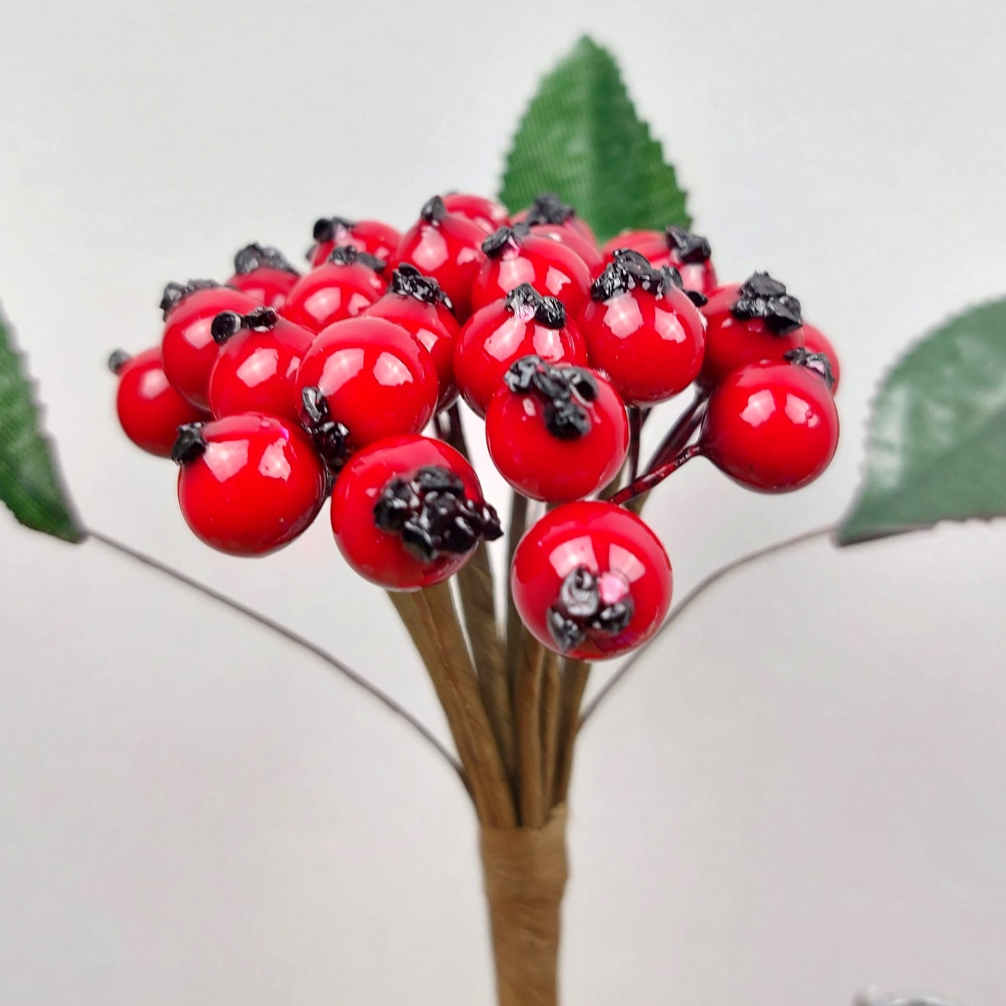 Bouquet of artificial red berries with green leaves on a light gray background