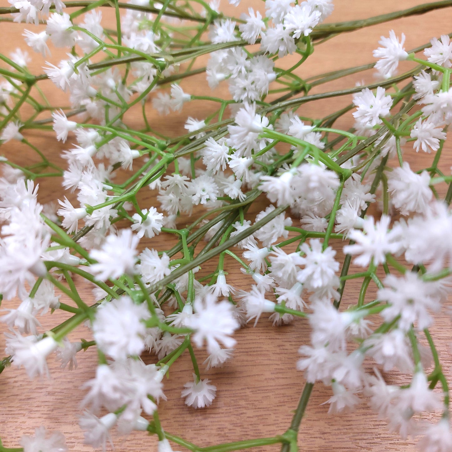 Close-up of artificial white flowers with green stems on a wooden surface