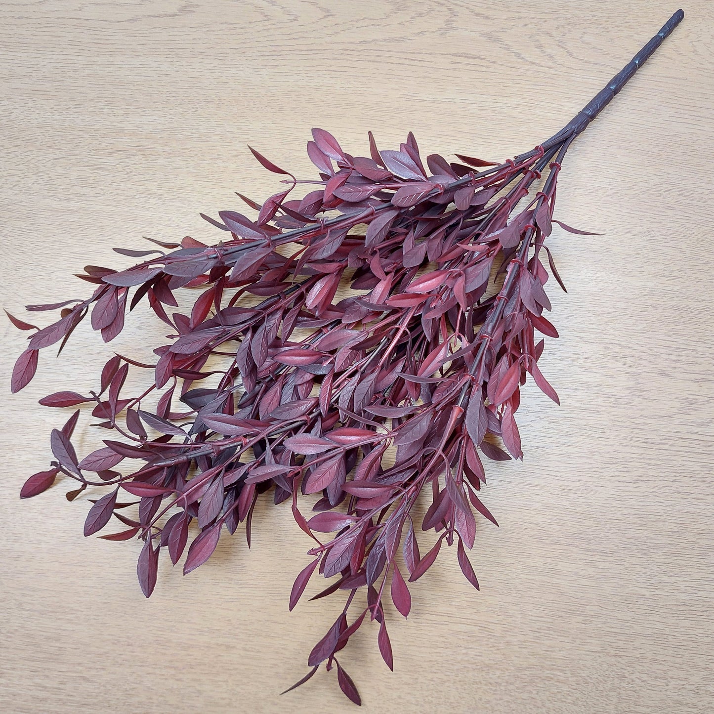 Artificial red and burgundy huckleberry leaf branch on a light wooden surface