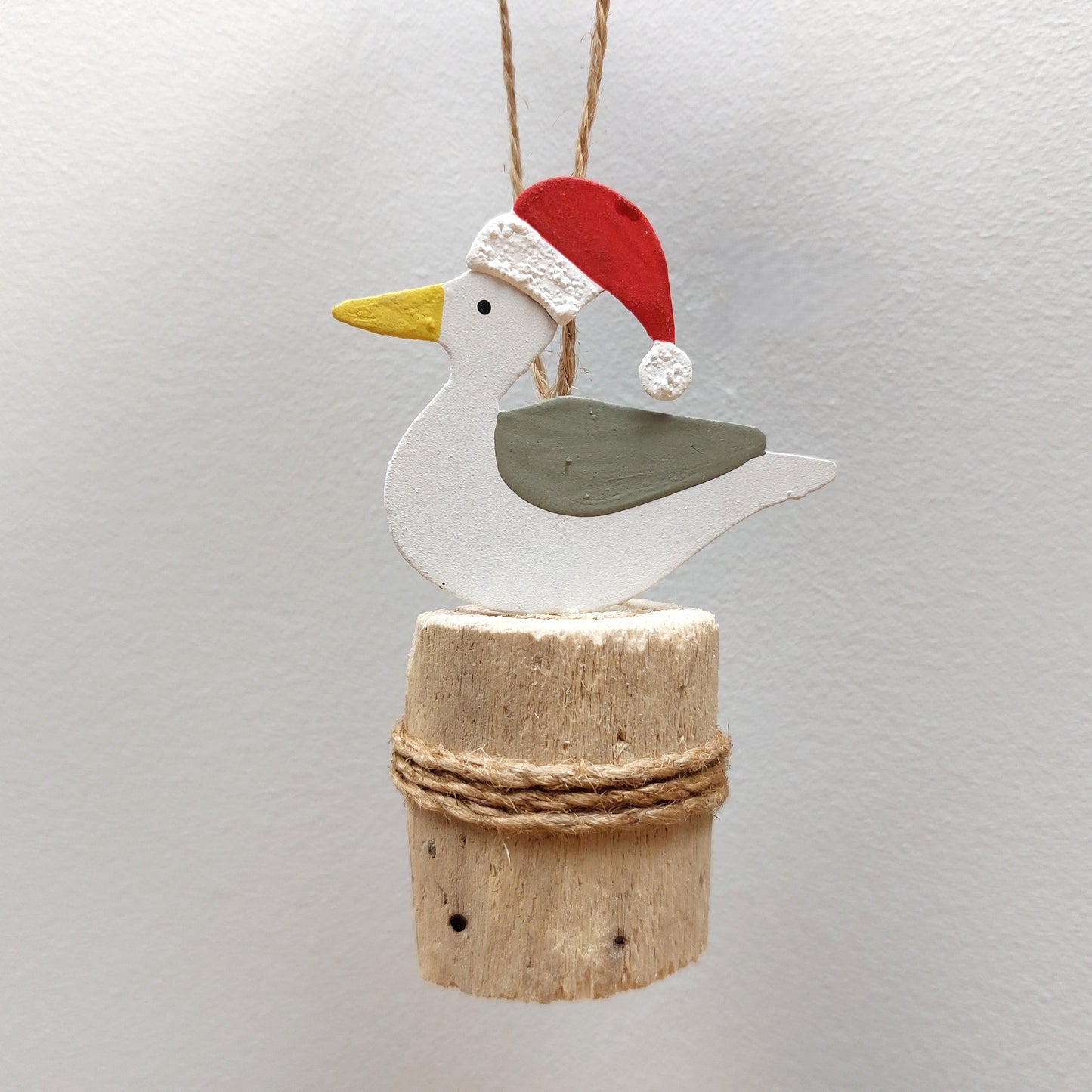 A metal seagull wearing a christmas hat on a wooden groyne against a grey background