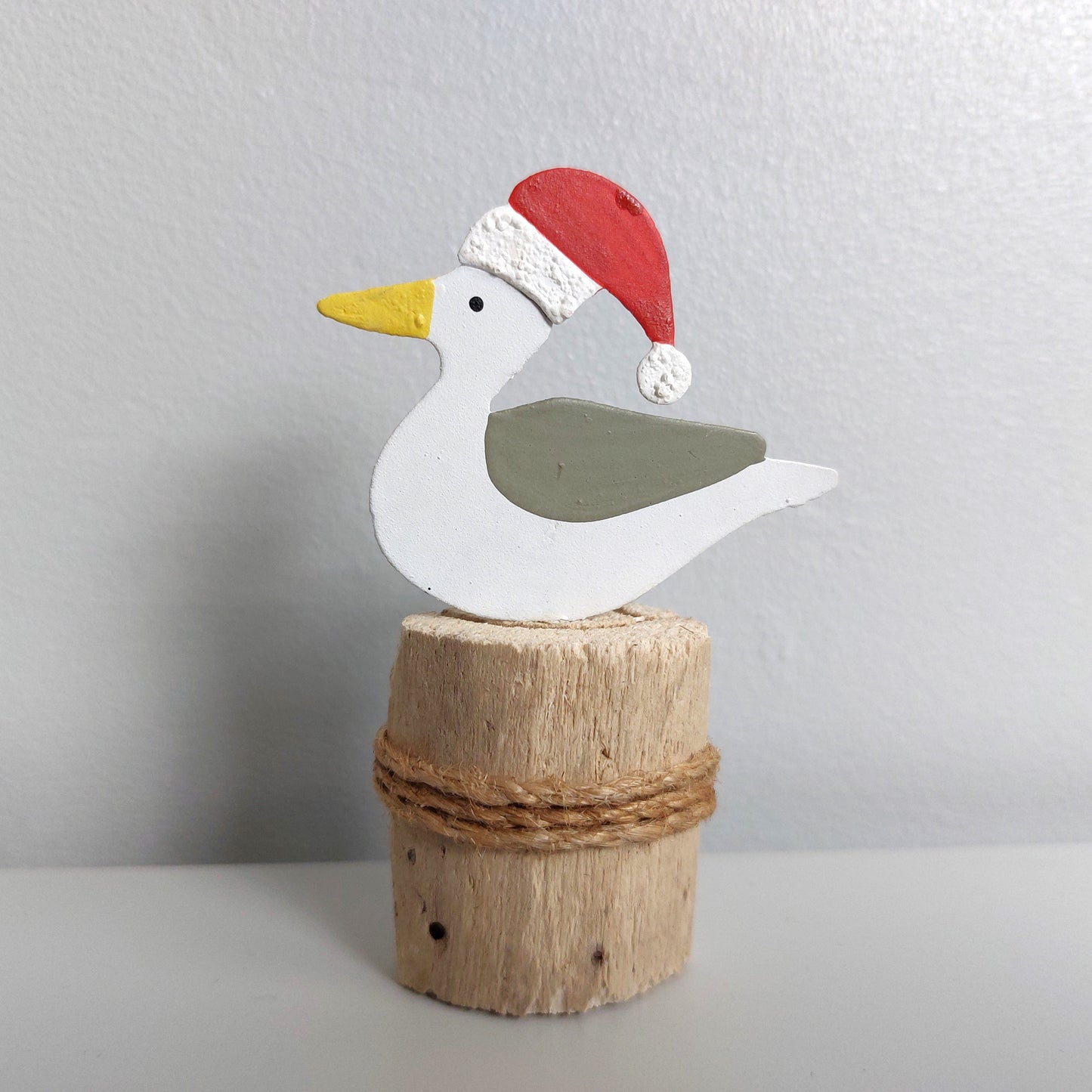 A tin seagull sitting on a wooden groyne against a pale background