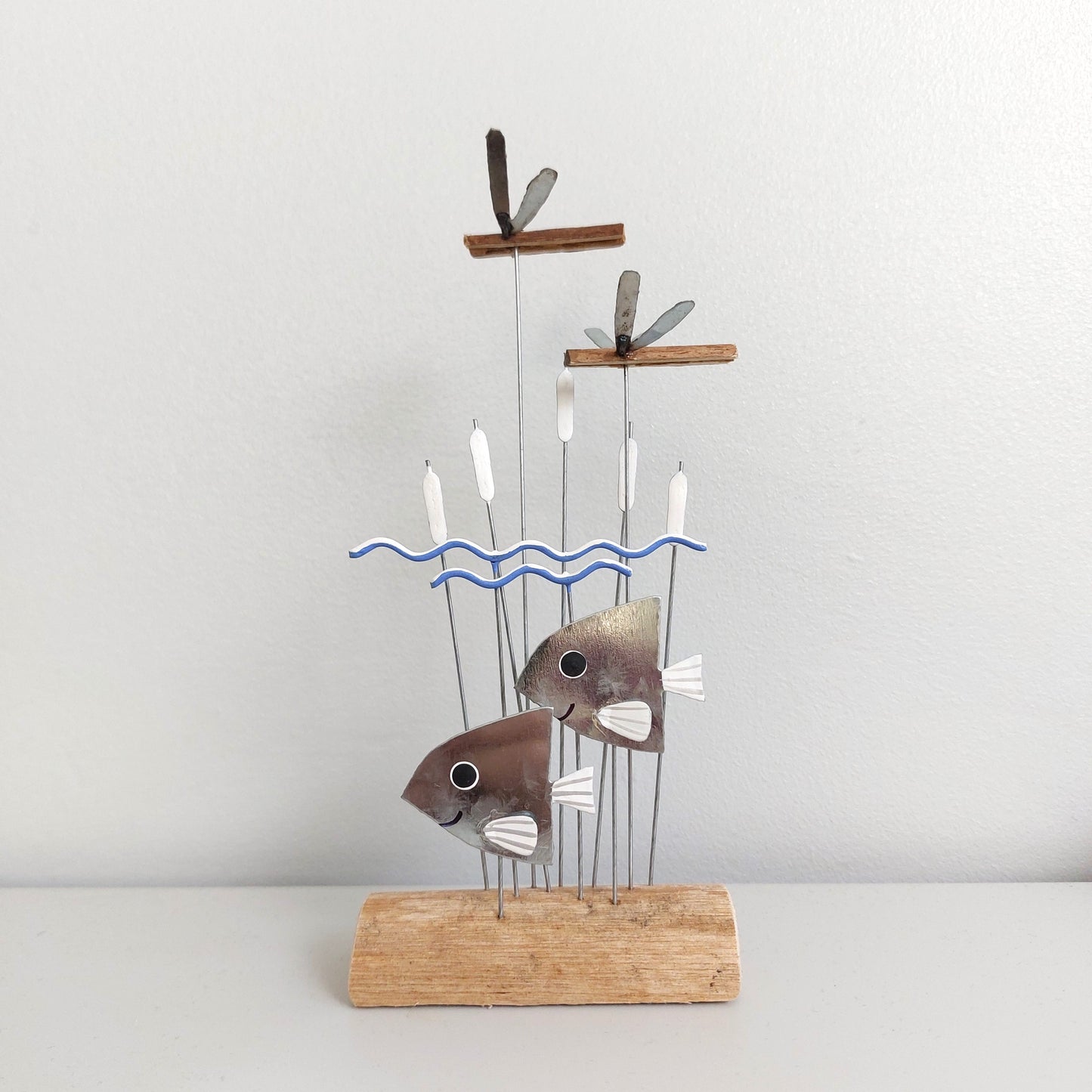 Decorative sculpture of fish on a stand with a wavy line design against a plain background