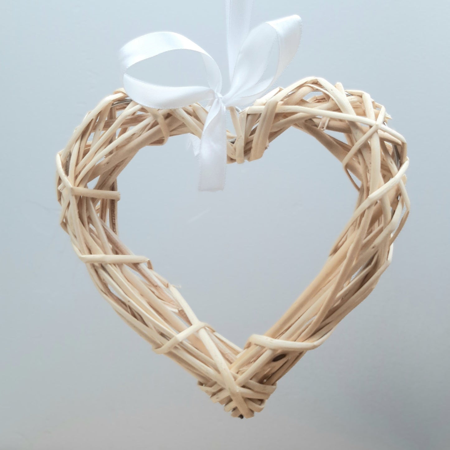 A hanging Natural Colour Wicker Heart with a white satin ribbon and bow.