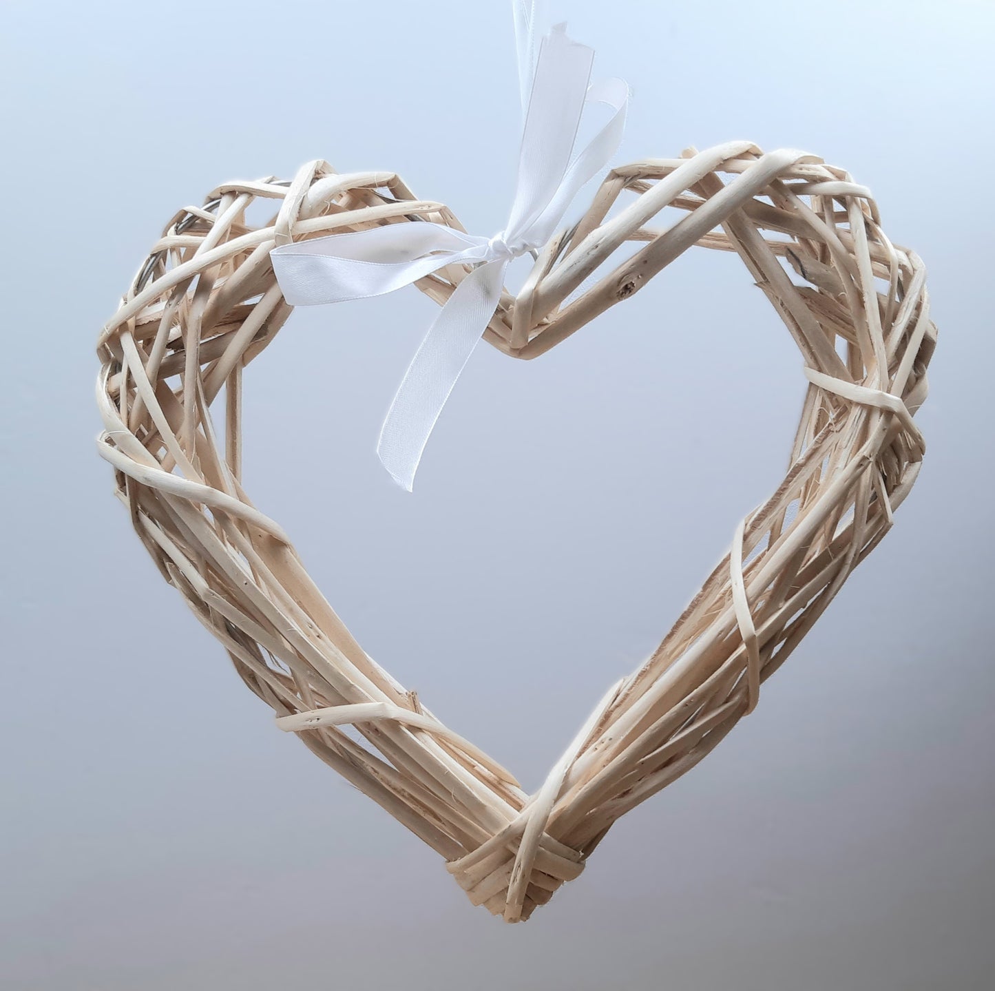 A hanging Natural Colour Wicker Heart with a white satin ribbon and bow.