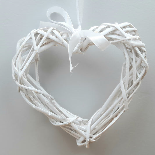 A hanging White Colour Wicker Heart with a white satin ribbon and bow.