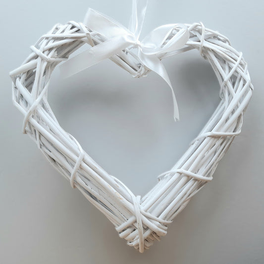 A hanging White Colour Wicker Heart with a white satin ribbon and bow.