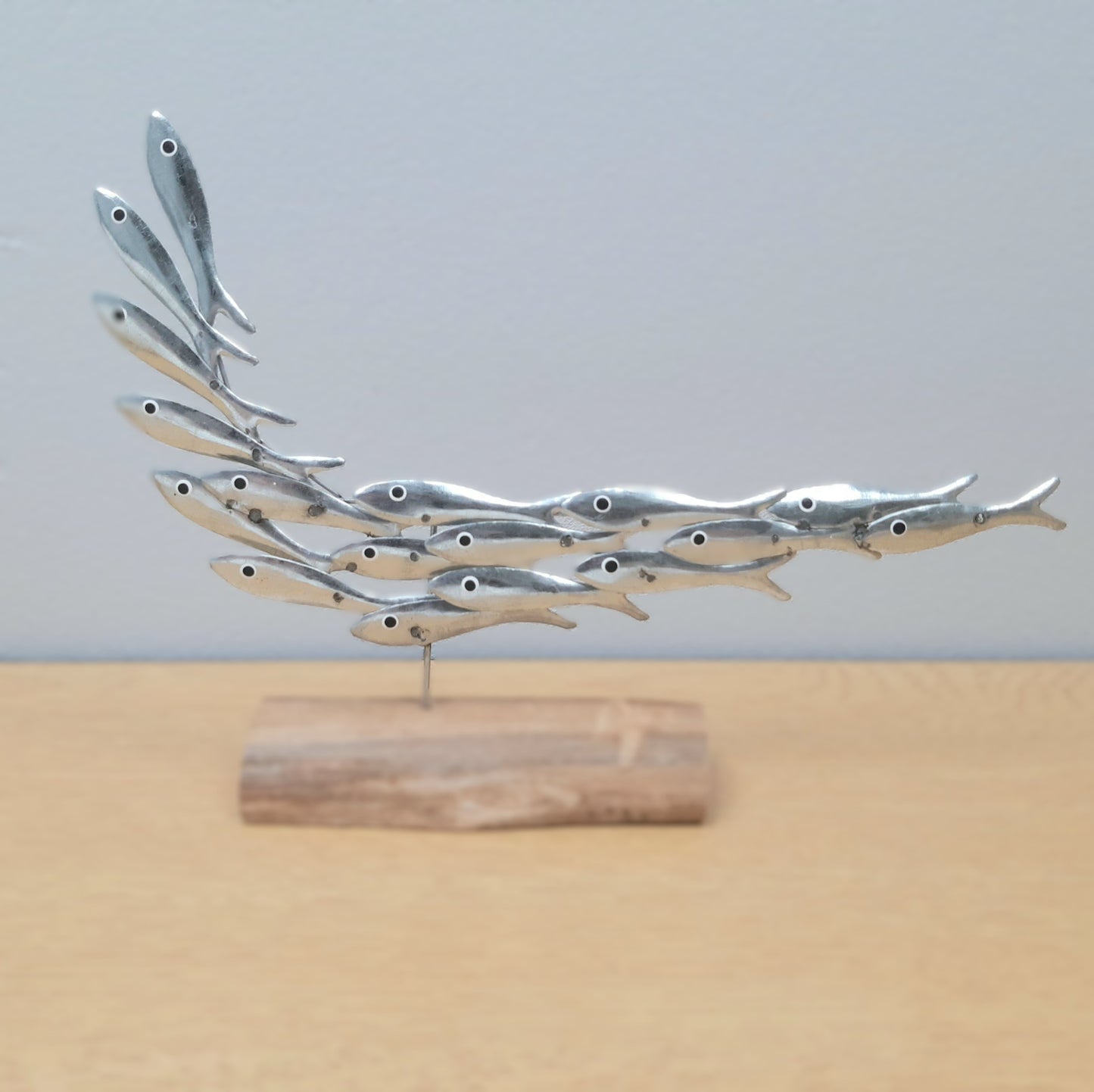 Metallic fish sculpture on a wooden base against a light gray background
