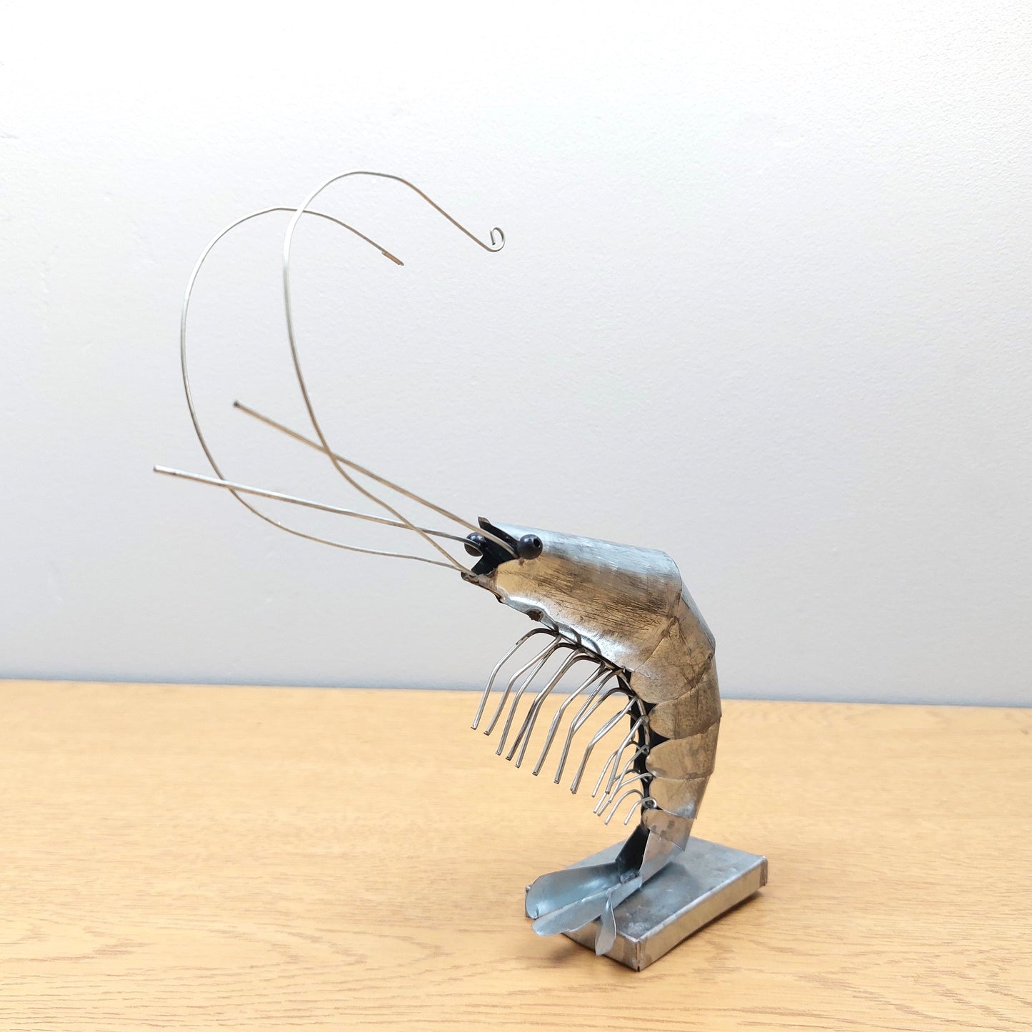 Metallic shrimp sculpture on a wooden surface with a plain background