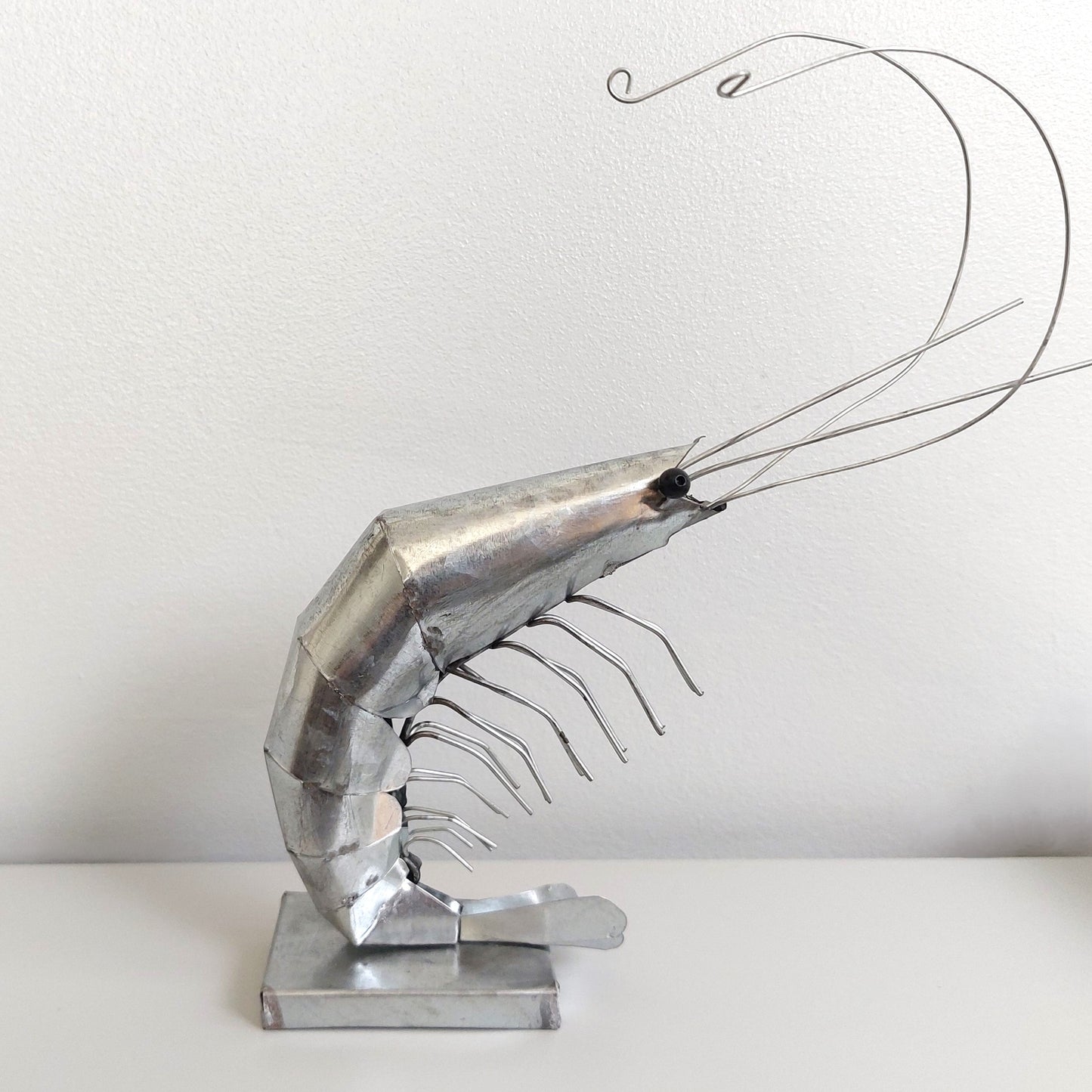 Metallic shrimp sculpture on a white surface with a plain background