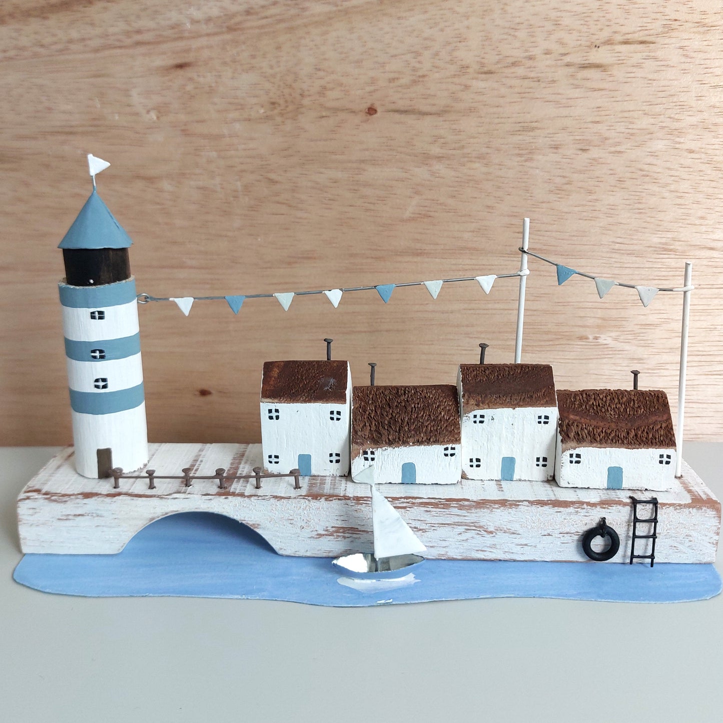 Model of a coastal scene with a lighthouse, houses, and a sailboat on a wooden background