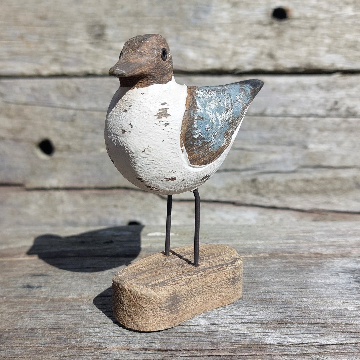 Decorative Sanderling wooden bird sculpture with metal legs on a wooden base against a wooden background