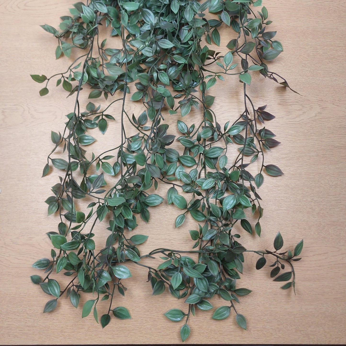 Green leafy artificial ruscus vine garland with dark brown stems laid out on a light wood surface.