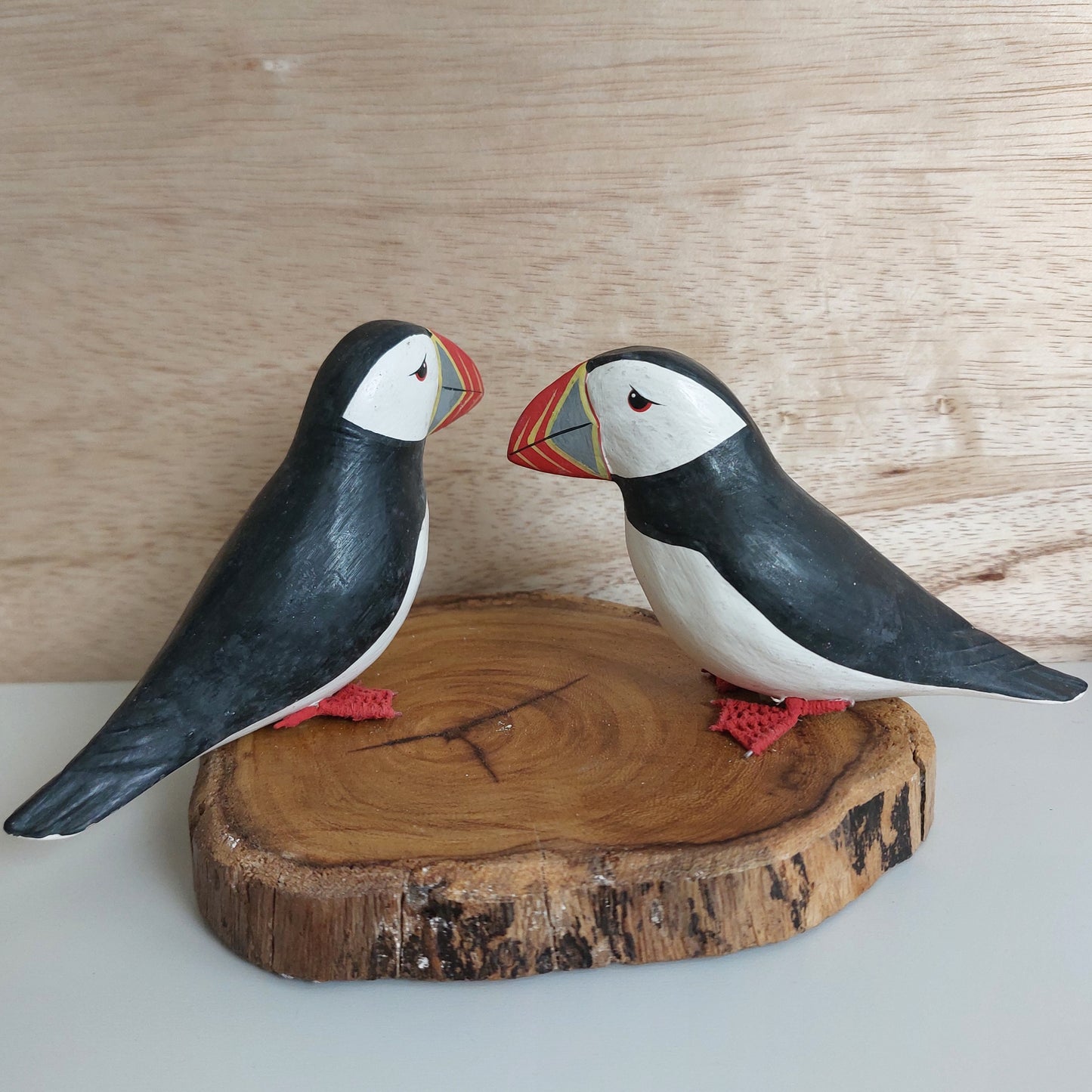 Two hand carved and painted wooden puffin figurines on a wooden base against a wooden background