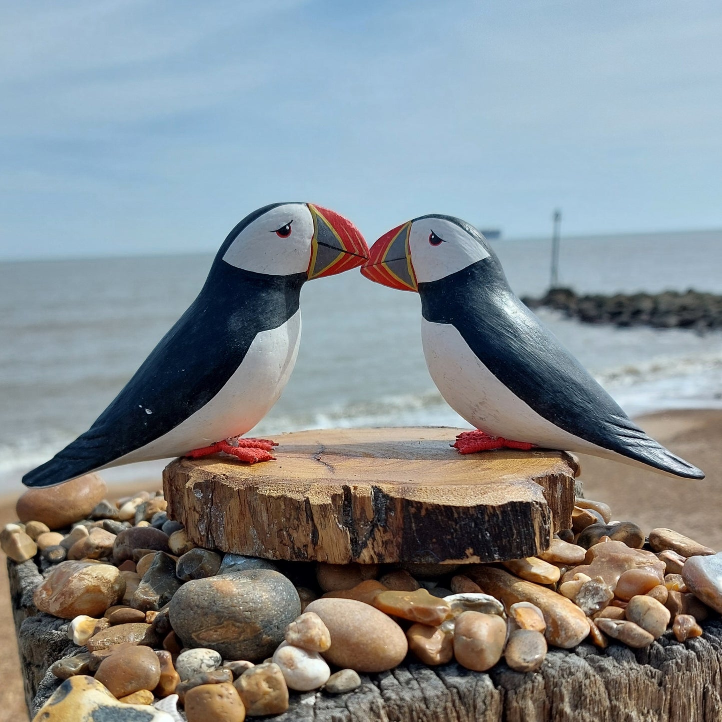 Two decorative puffins on a wooden platform with a beach and ocean in the background