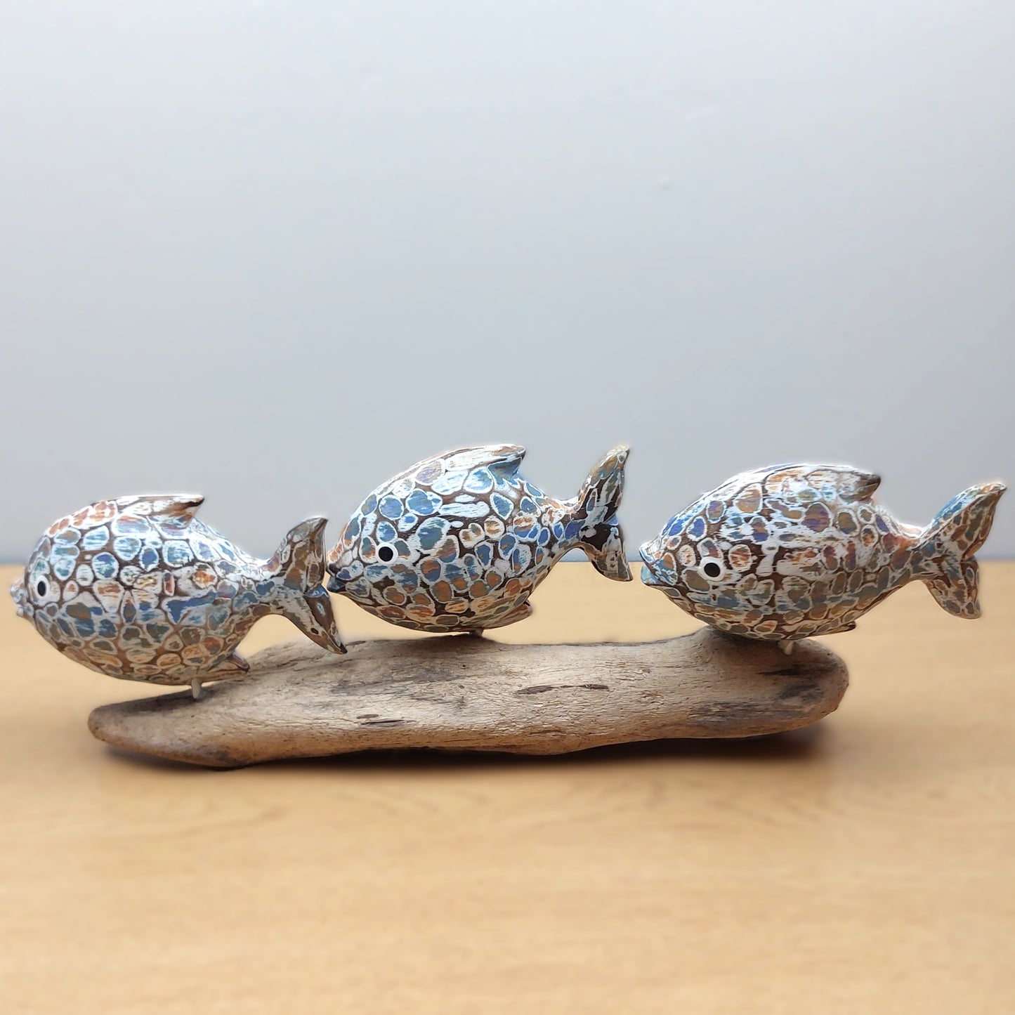 Decorative hand made and painted fish sculpture on a piece of driftwood made in Bali with a plain background