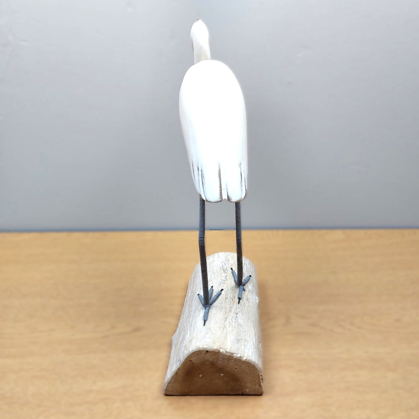 White handmade Egret bird figurine on a wooden base against a gray background