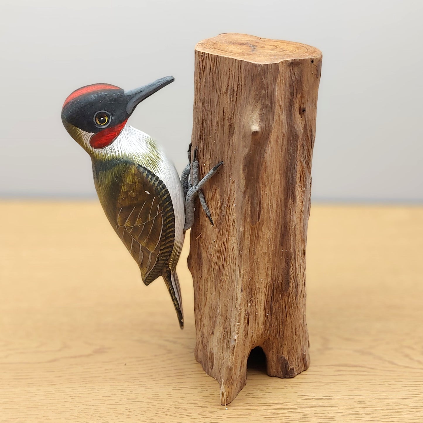 An ornate wooden hand carved and painted Green Woodpecker ornament from Bali, against a wooden background.