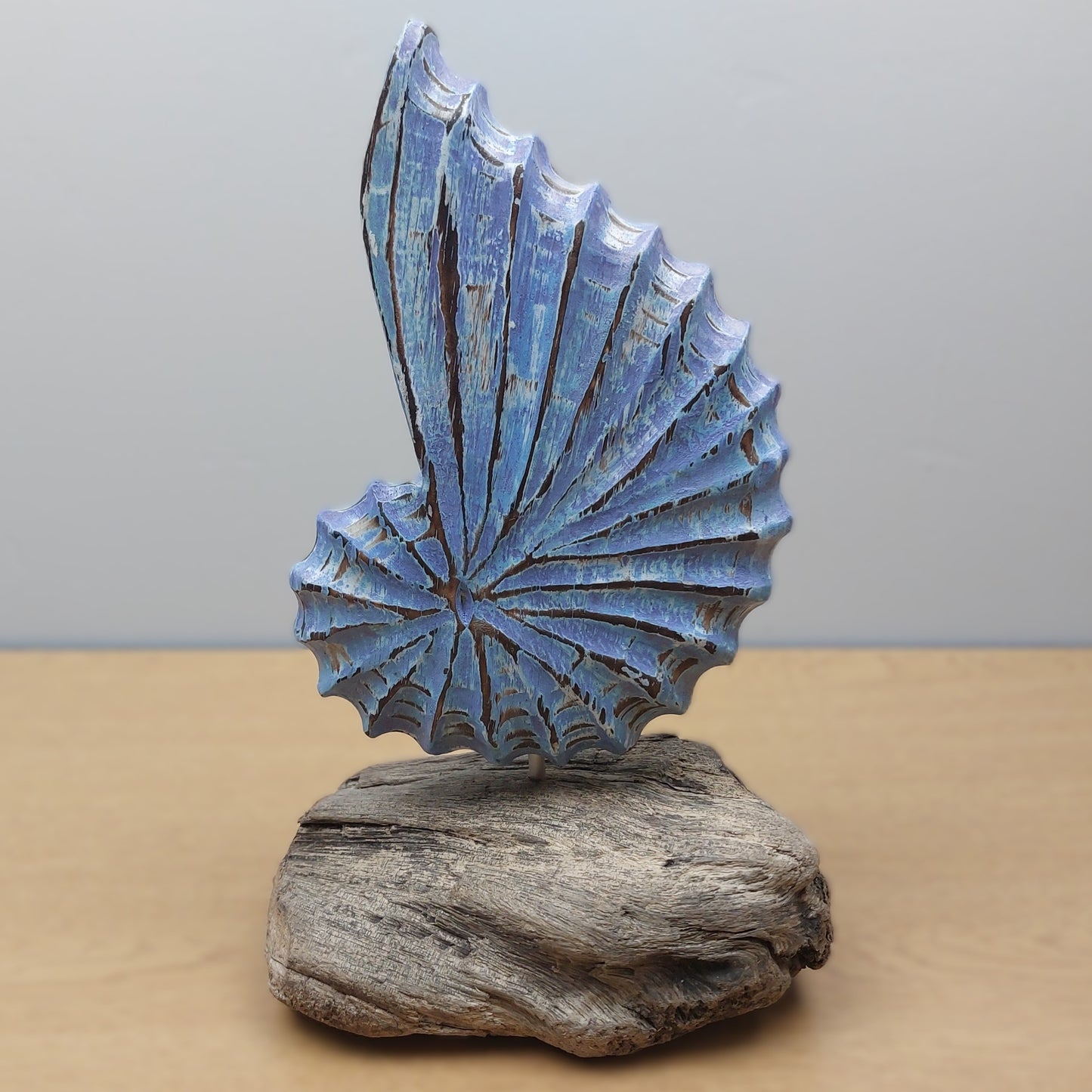 Blue wooden hand crafted in Bali sculpture on a wooden driftwood base against a gray background