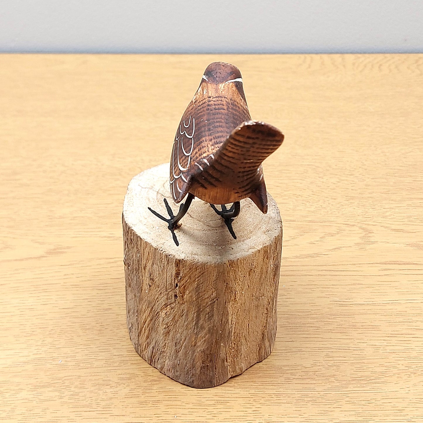 Wooden Handmade and painted Wren bird figurine on a wooden log block against a beige background.