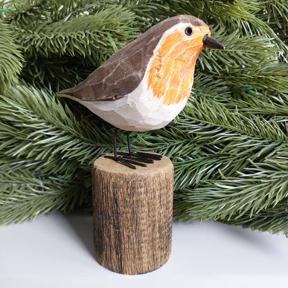 Decorative robin bird figurine on a wooden stand with green faux foliage in the background