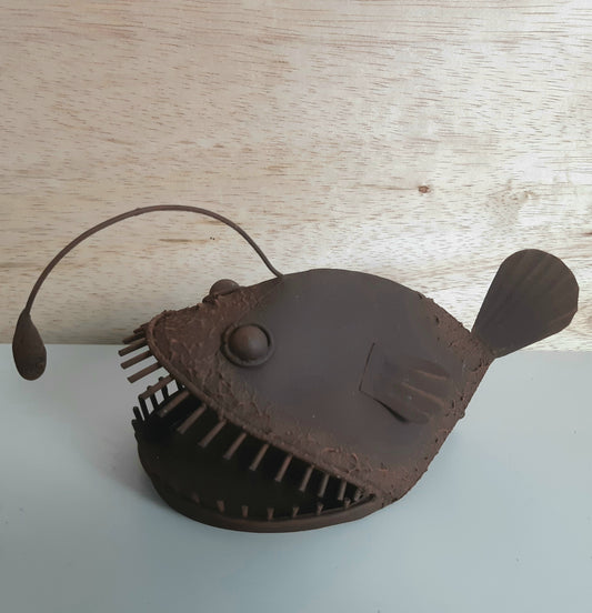 Rust style anglerfish metal model on a light wooden surface
