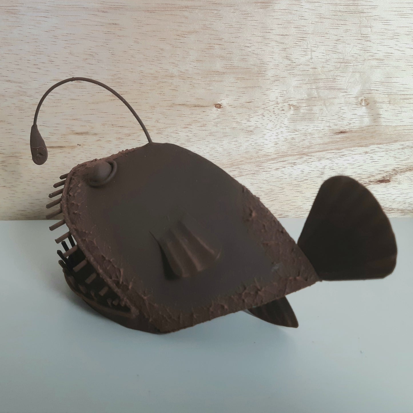 Brown rust style Allan the Angler Fish figurine on a light wooden surface