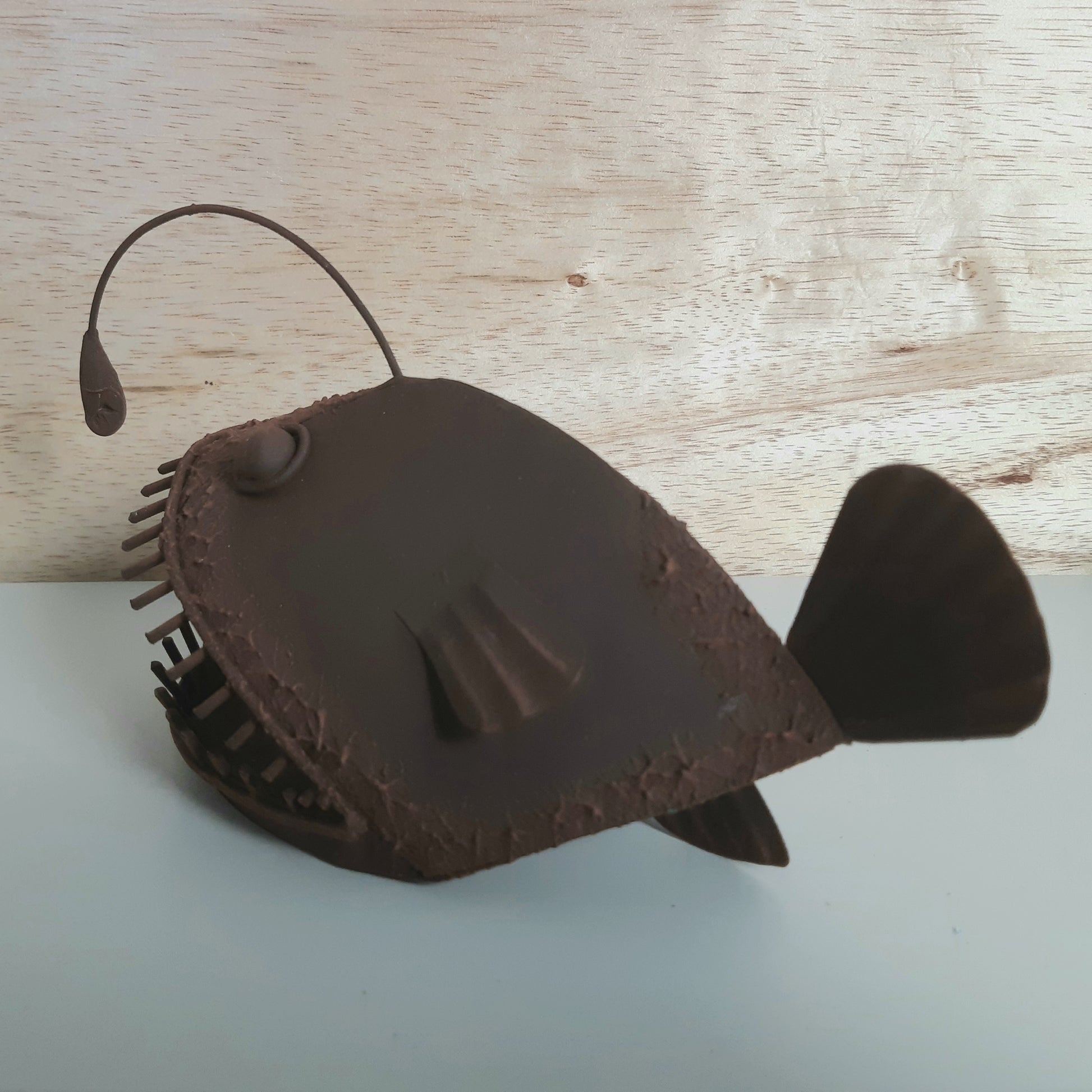 Brown rust style Allan the Angler Fish figurine on a light wooden surface