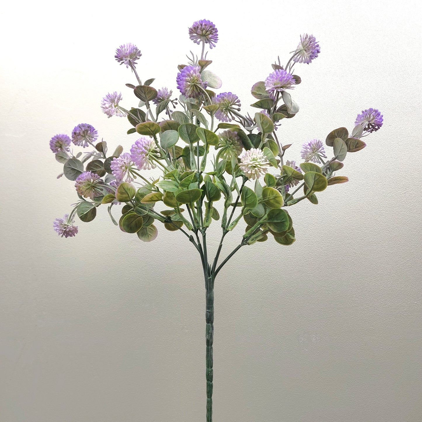 An artificial flower stem featuring purple thistle-like blooms and green eucalyptus leaves on a plain light background.