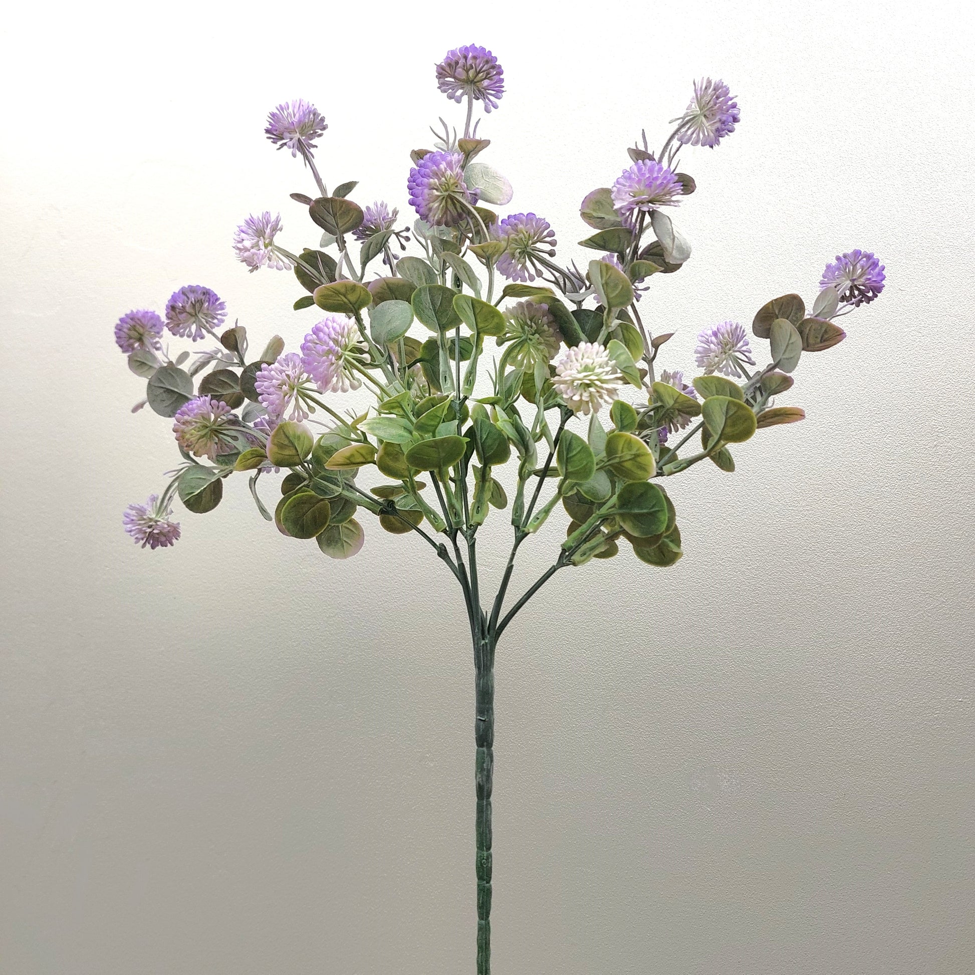 An artificial flower stem featuring purple thistle-like blooms and green eucalyptus leaves on a plain light background.