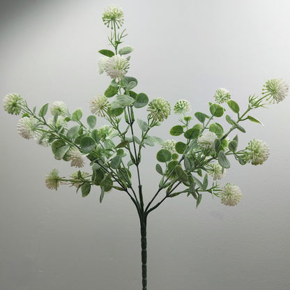 An artificial flowering branch with round white and green globe thistle flowers and green oval leaves on a dark stem, photographed against a plain light gray background.