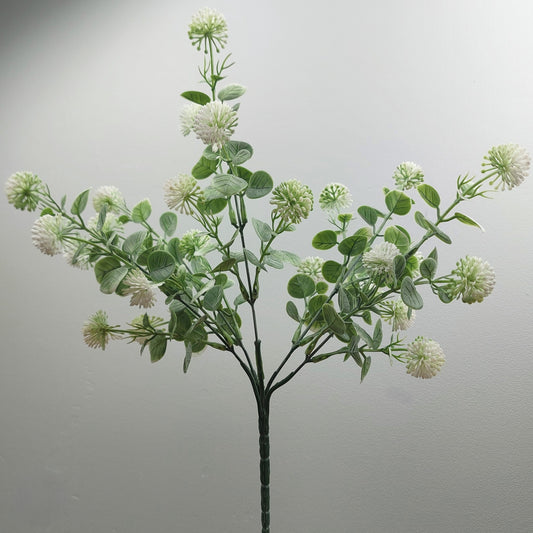 An artificial flowering branch with round white and green globe thistle flowers and green oval leaves on a dark stem, photographed against a plain light gray background.