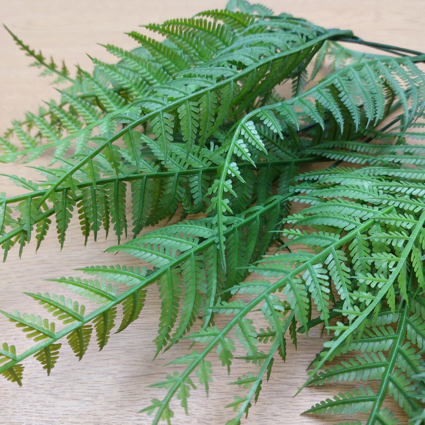 Green artificial fern fronds close up against a light wood background.