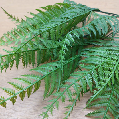 Green artificial fern fronds close up against a light wood background.