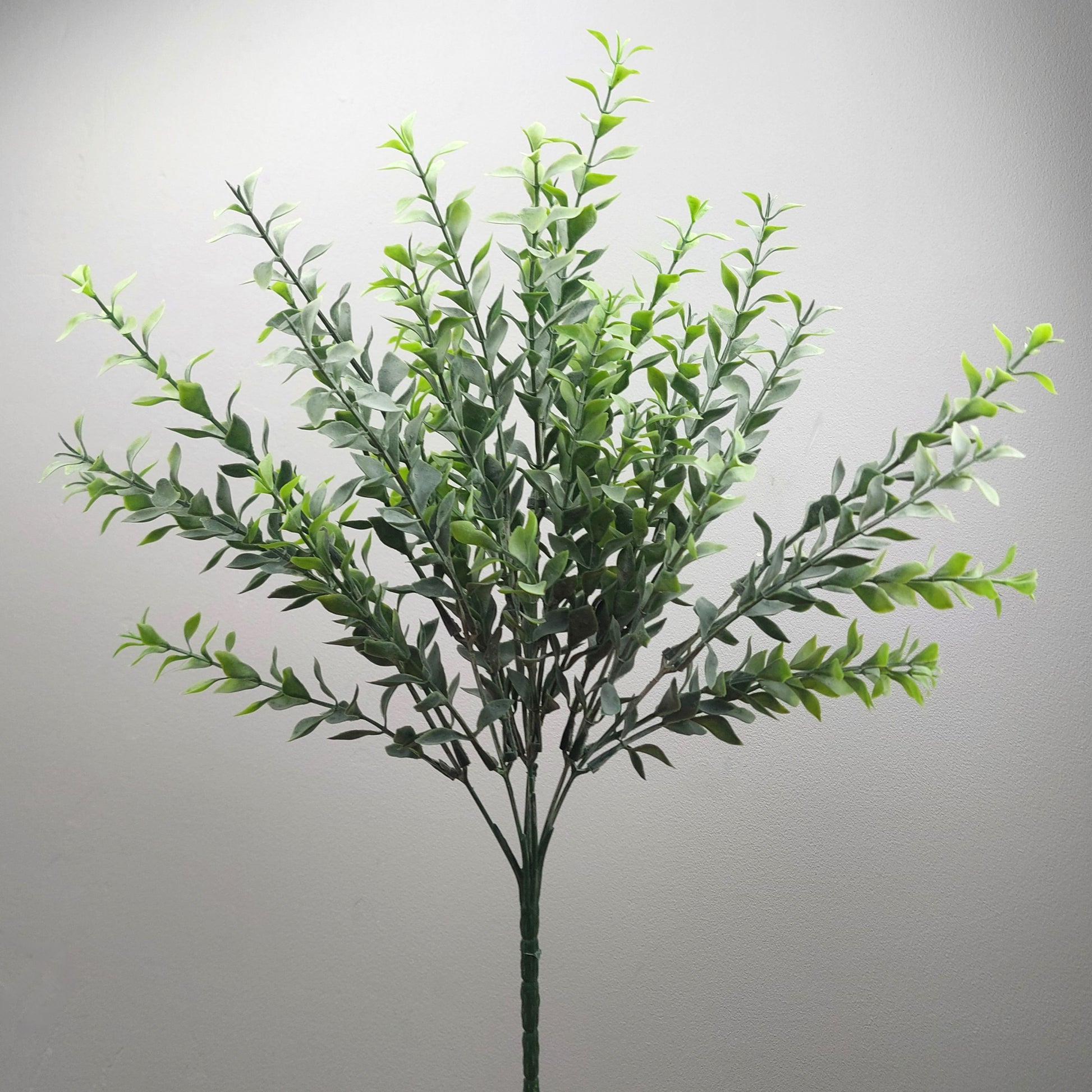 An artificial green leafy Parvifolia spray with multiple stems and small oval leaves, photographed against a plain light gray background.