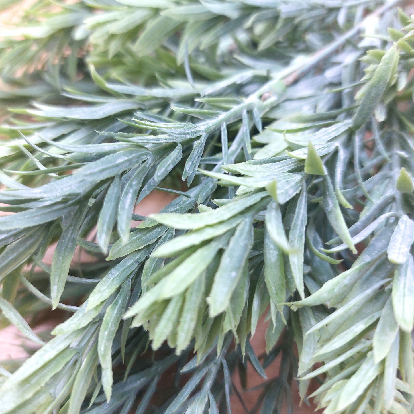 Close-up of an artificial green needle-like evergreen branch with dense, slender leaves.