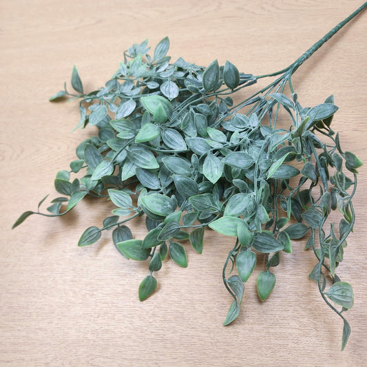 Artificial green leafy ruscus stem with multiple stems and small oval leaves, arranged on a light wood surface.