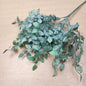 Artificial green leafy ruscus stem with multiple stems and small oval leaves, arranged on a light wood surface.